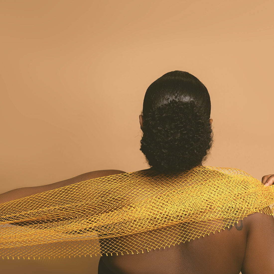 A woman viewed from the back with a Bellanomi yellow African exfoliating net sponge draped over their shoulders.