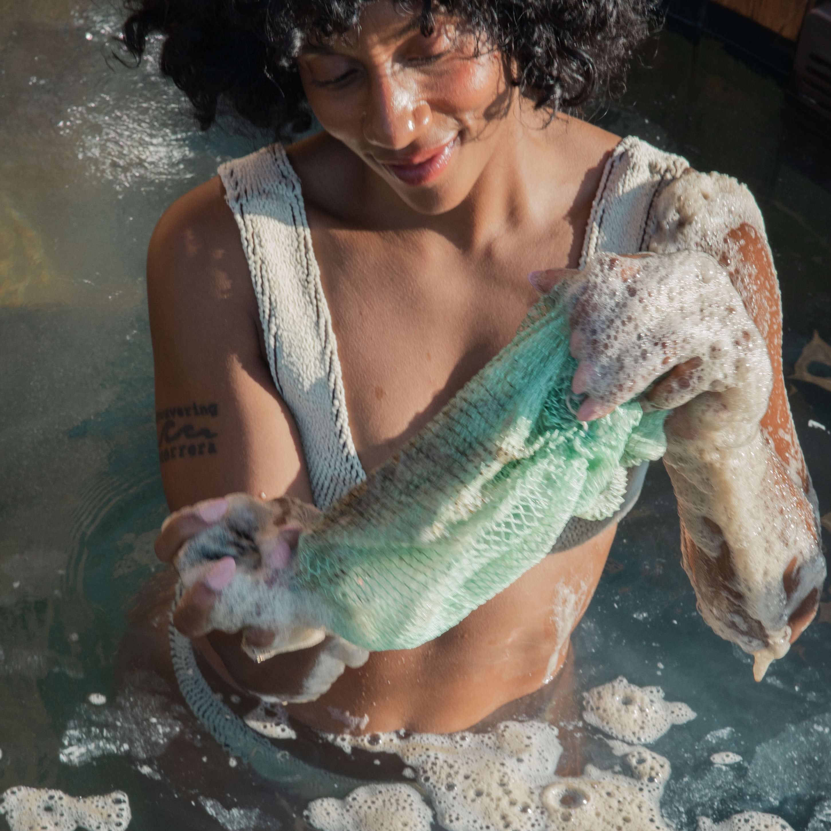 Woman in a bath with Bellanomi African net sponge with soap suds.