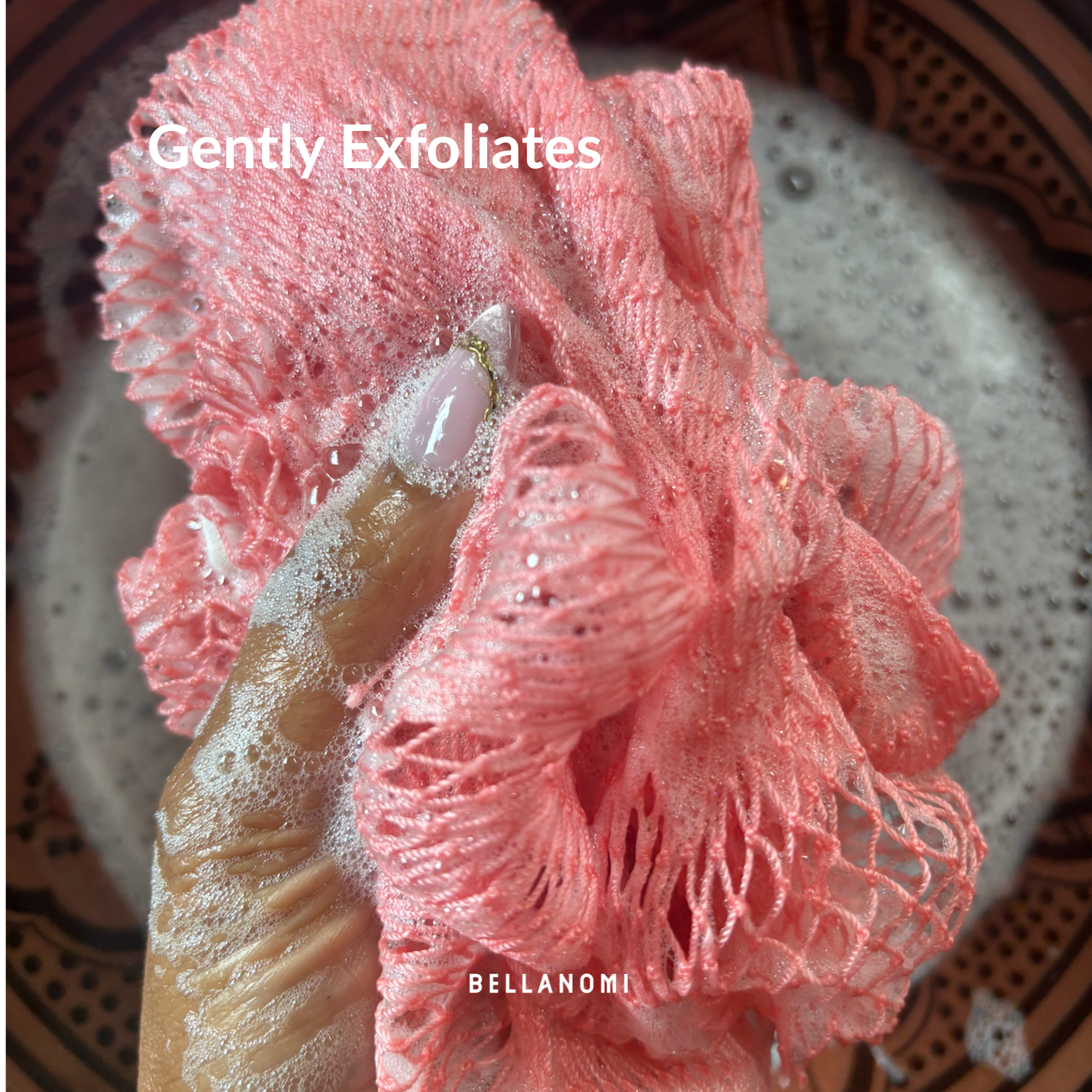 Pink exfoliating glove with a scrubber on a textured surface, featuring the brand &