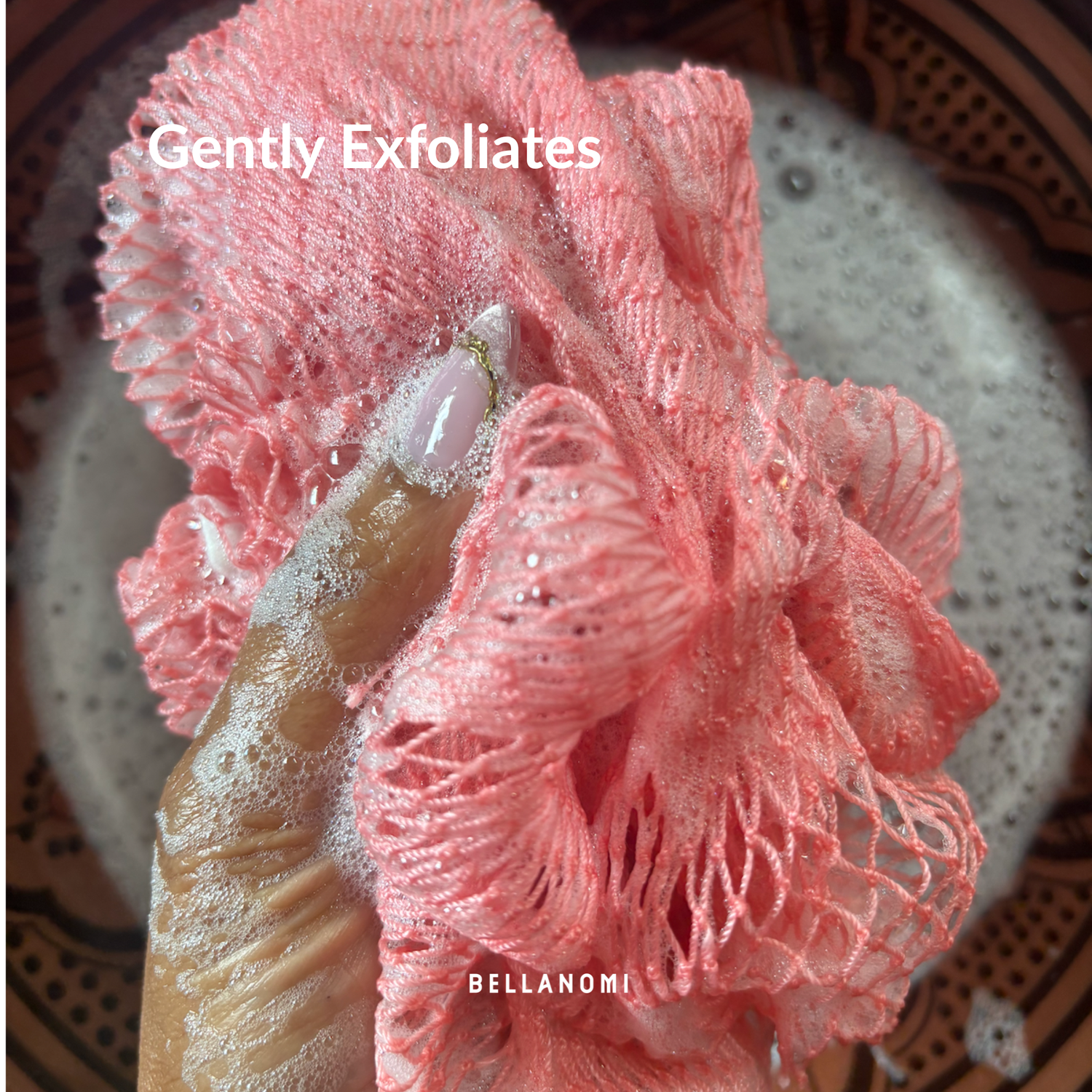 Pink exfoliating glove with a scrubber on a textured surface, featuring the brand &